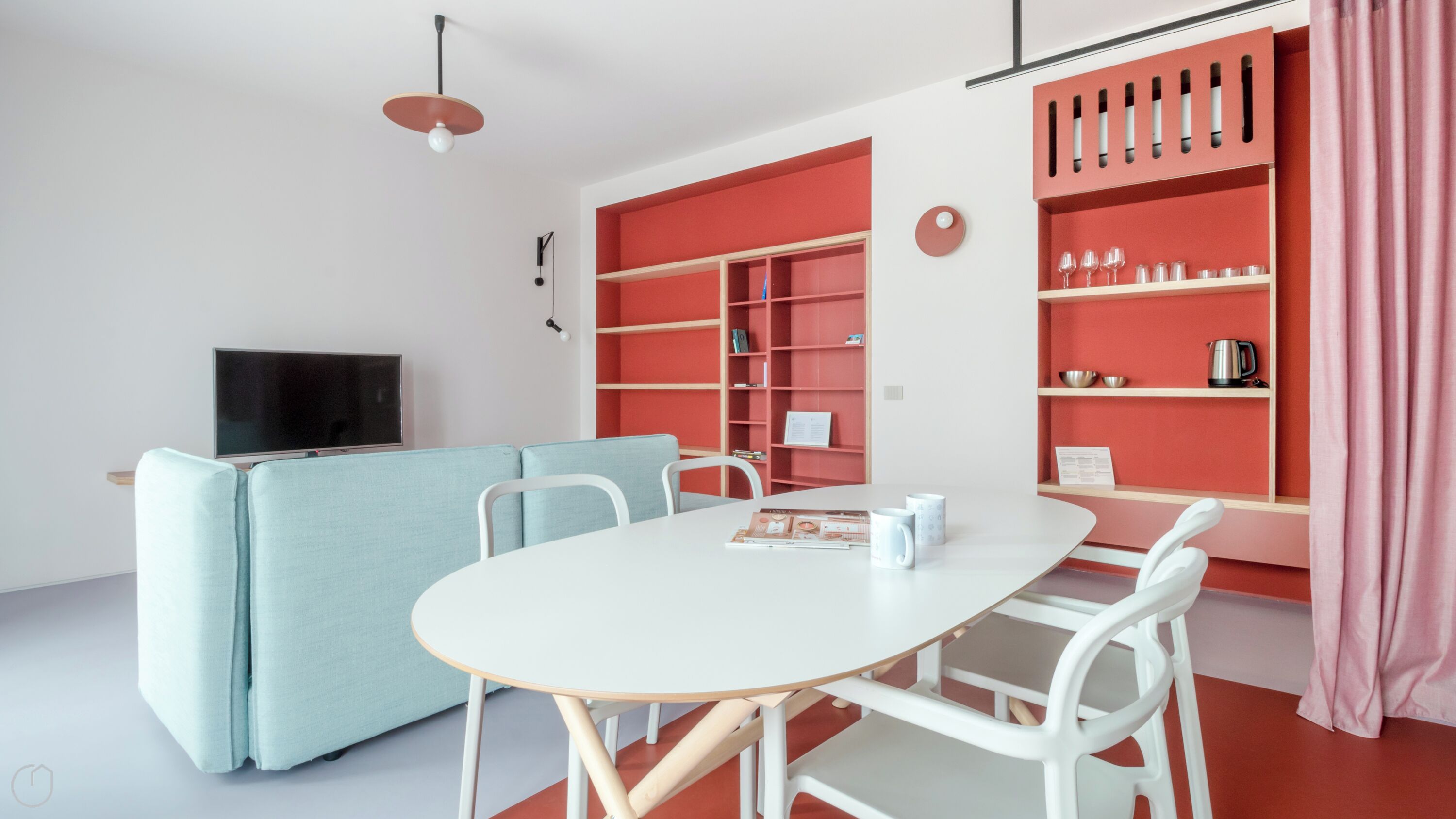 A modern living room with a white table, blue sofa, and red shelving units.