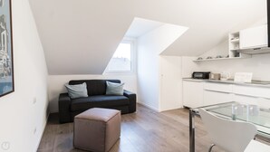 A modern loft apartment with a loft bed, a small kitchenette, a glass dining table, and a gray sofa with cushions. - Italianway - Corso Como 9 (Milan)