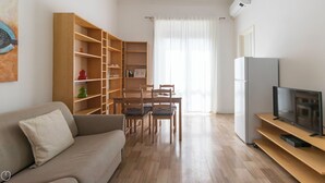 Una sala de estar con un sofá, una mesa de comedor con sillas, una estantería y un televisor sobre un mueble.