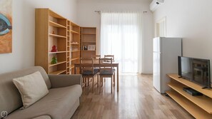 A living room with a sofa, a dining table with chairs, a bookshelf, and a TV on a stand. - Italianway - Argonne 7 (Milan)