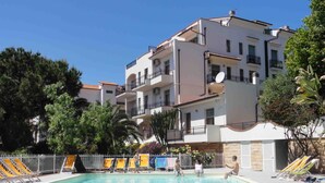 A swimming pool with a white building in the background. - Residenza dei Fiori - by Mamberto S.r.l. (Pietra Ligure)