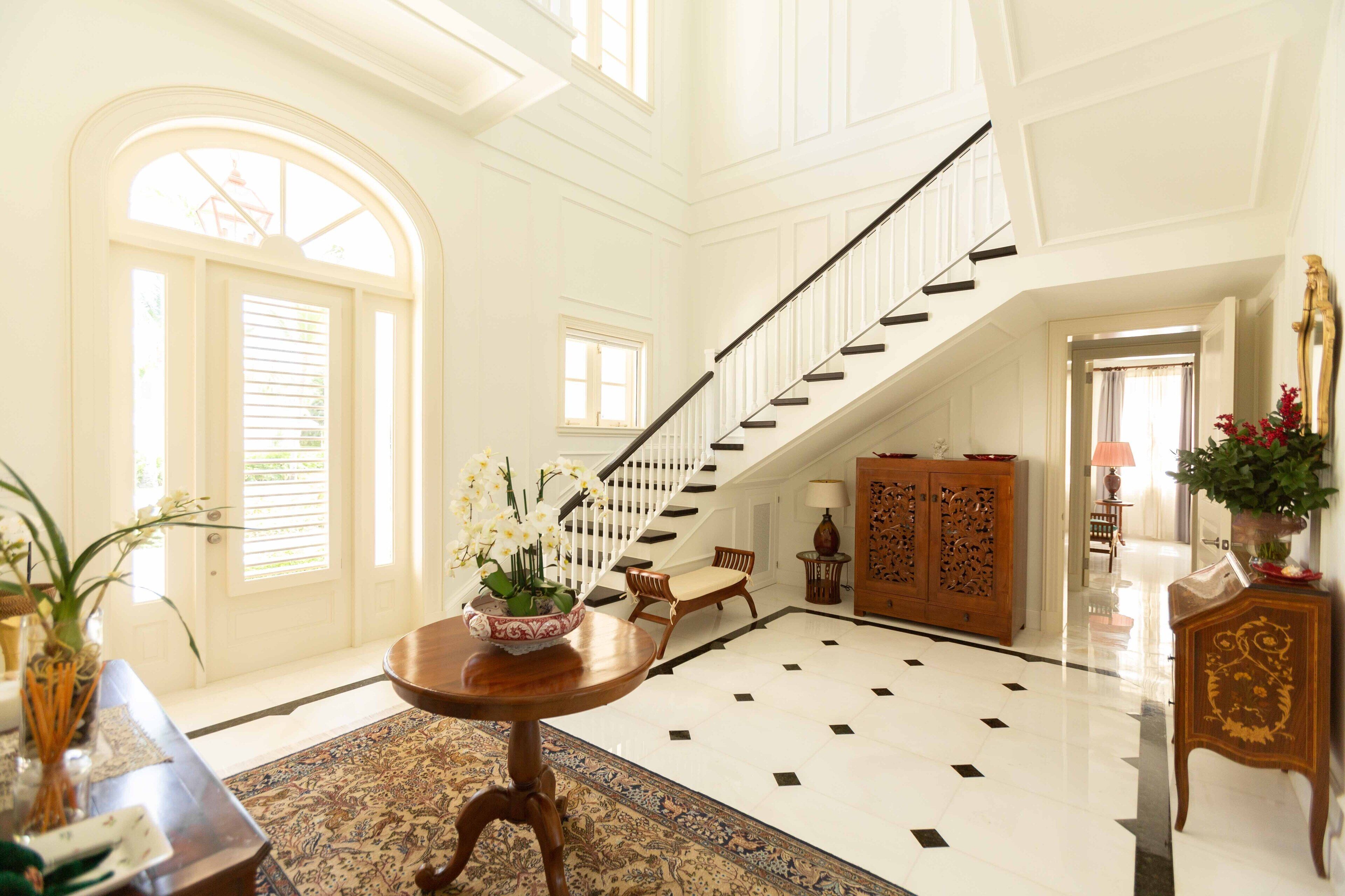 Un hall d’entrée spacieux avec un plafond haut, un grand escalier et une grande armoire en bois.