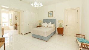 A bedroom with a large bed, a chandelier, white walls, and a door. - Luxury Golf View Villa in Punta Cana Resort & Club with Private Pool and Jacuzzi (Punta Cana)