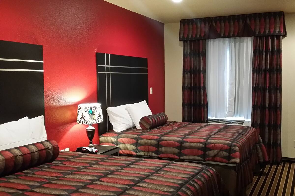 Une chambre d’hôtel avec deux lits, une table de chevet, une lampe et une fenêtre avec des rideaux.