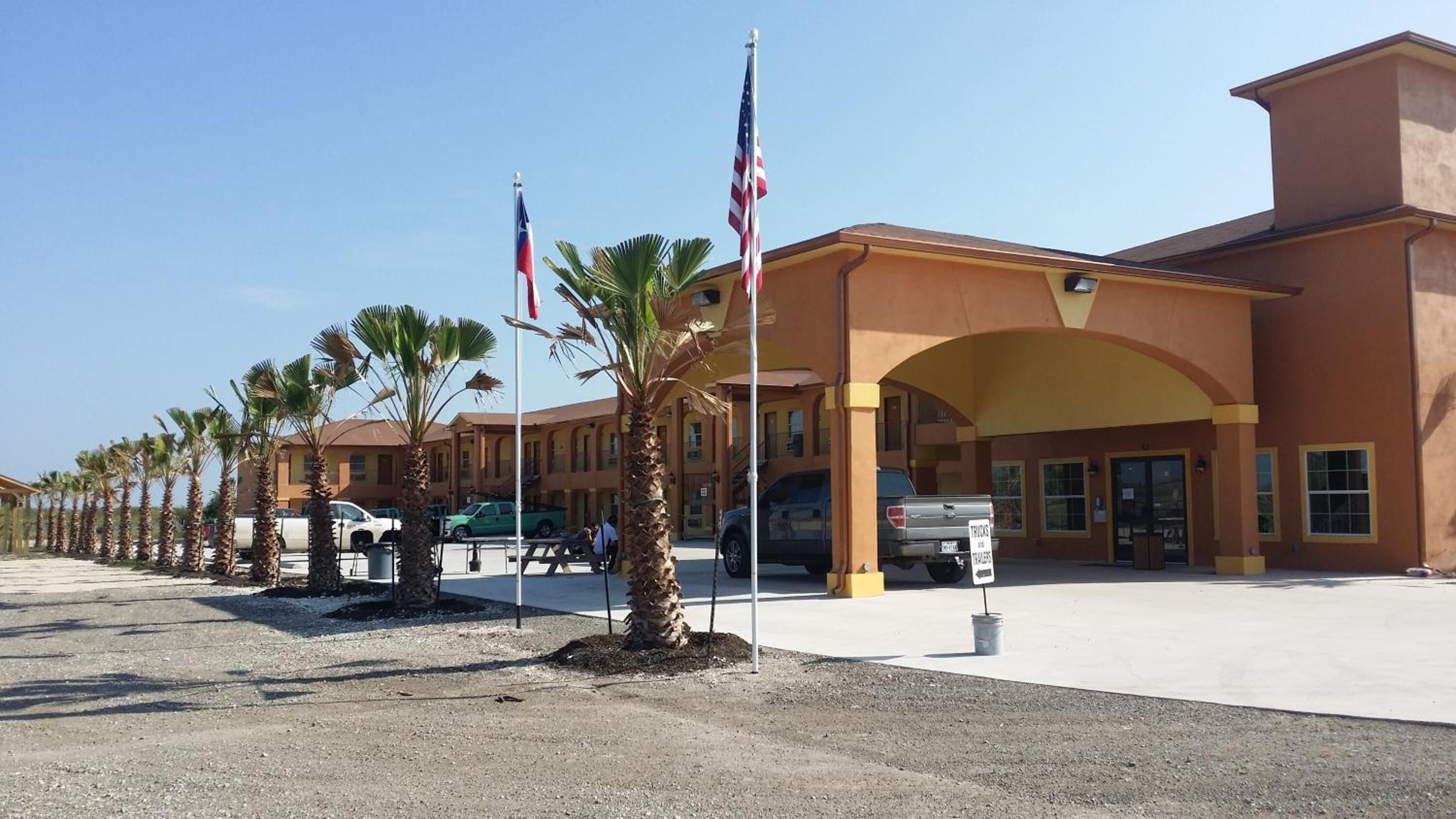 Un hotel con una entrada amplia, palmeras y banderas estadounidenses.
