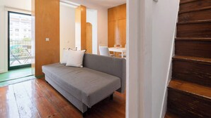 A room with a grey sofa, wooden floor, and a staircase.
