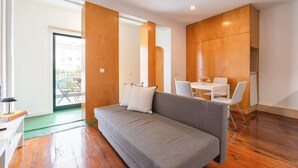 A modern living room with a grey sofa, white chairs, a small table, and wooden paneling.