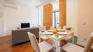 A modern dining area with a white table, chairs, and a grey sofa.