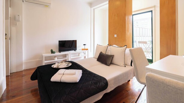 A modern hotel room with a bed, a TV, a wooden accent wall, and a balcony view.