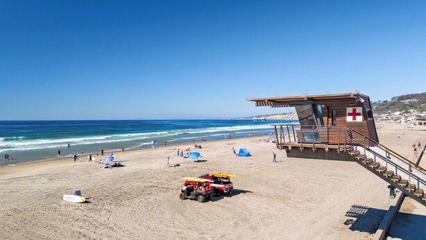 Une plage avec une tour de surveillance pour les sauveteurs, des parasols et un véhicule de sauvetage.