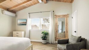Une chambre à coucher avec un lit, une chaise, un grand miroir, une fenêtre avec des rideaux et une plante en pot.