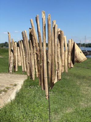 A wooden structure with a pointed top, possibly a decorative piece or part of a fence, set against a grassy field with a clear sky and distant water body. - View over the Loire. Le Futreau, gîte 8/9 pers (Chalonnes-sur-Loire)