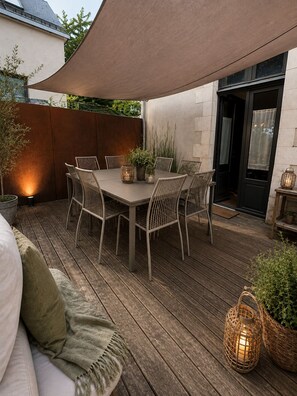 A wooden deck with a table and chairs, a covered area, and a door leading to a building.