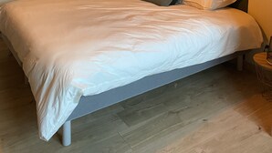 Een net opgemaakt bed met witte lakens, een gestructureerde wand erachter en een hanglamp erboven.