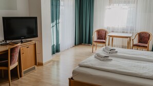 A hotel room with a bed, a television on a wooden cabinet, two chairs, a small table, and a window with curtains. - Georgshof (Podersdorf am See)