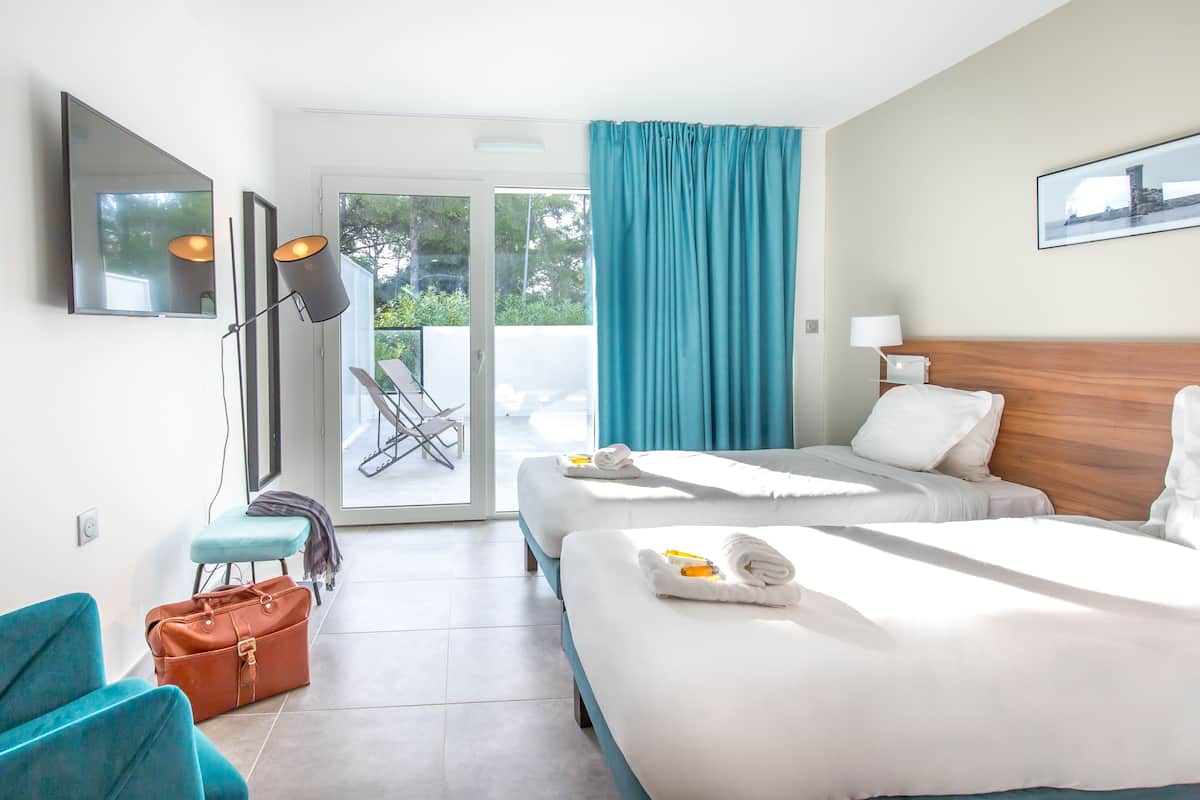 Habitación de hotel con dos camas, televisión, escritorio y vista al exterior.