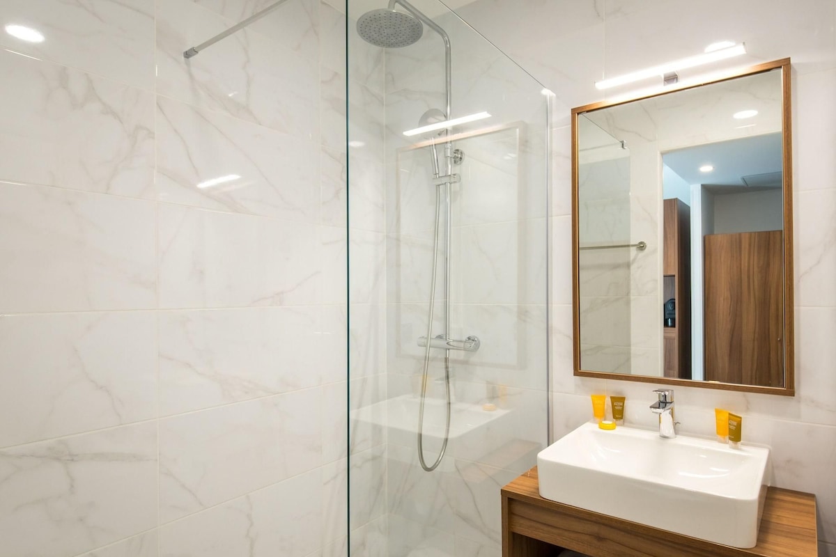 A modern bathroom with a glass-enclosed shower, a white sink with wooden vanity, and a large mirror.
