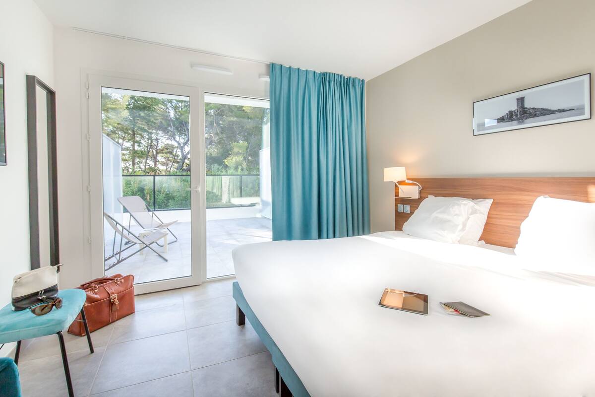 Habitación de hotel con cama, un escritorio con silla, una maleta y vistas al exterior.