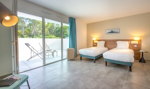 A hotel room with two beds, a sliding glass door to a balcony, a small table, and a chair.