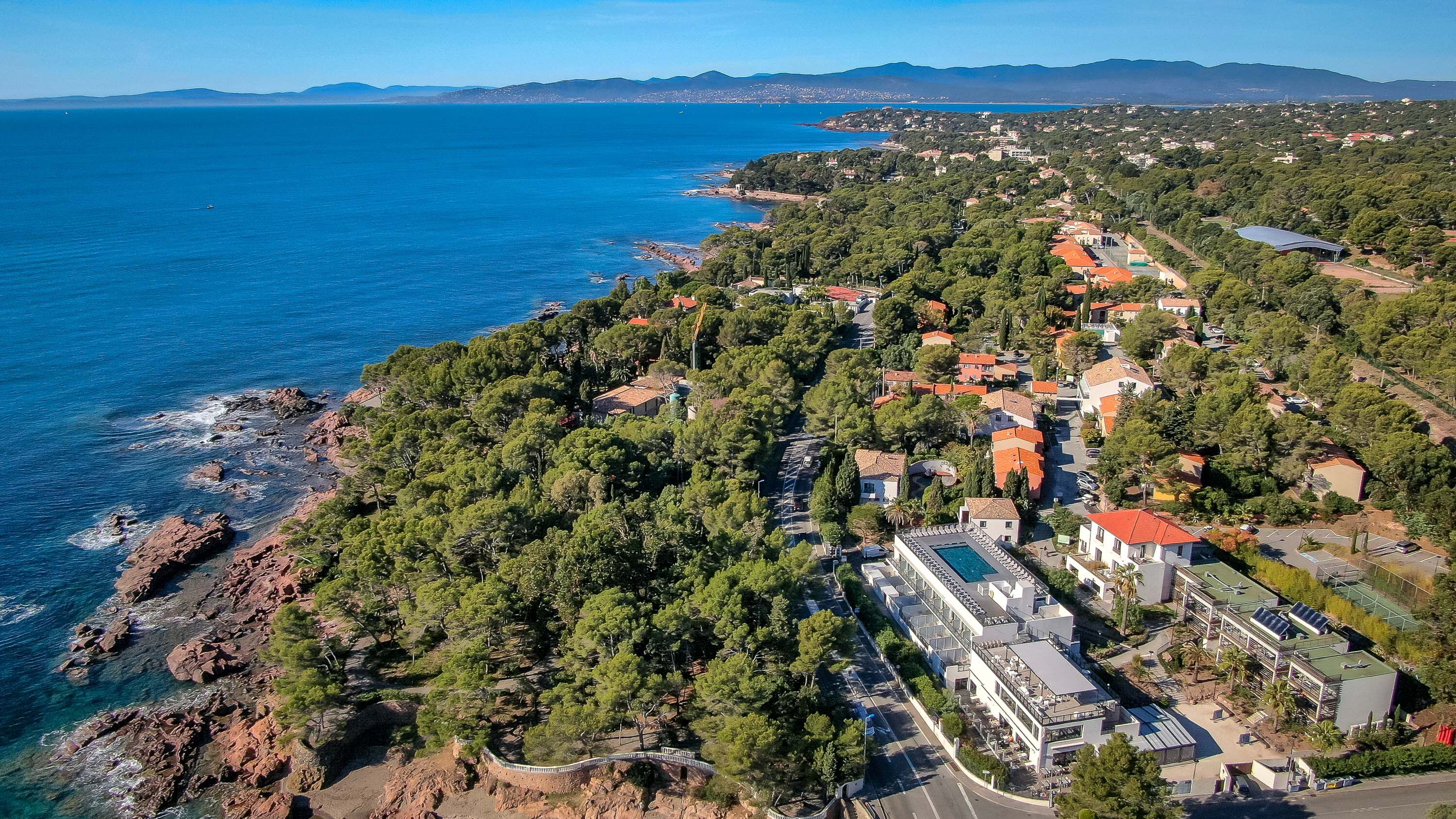 Vue aérienne d’une ville côtière, avec un mélange de bâtiments résidentiels, un grand complexe de piscines et une côte rocheuse.