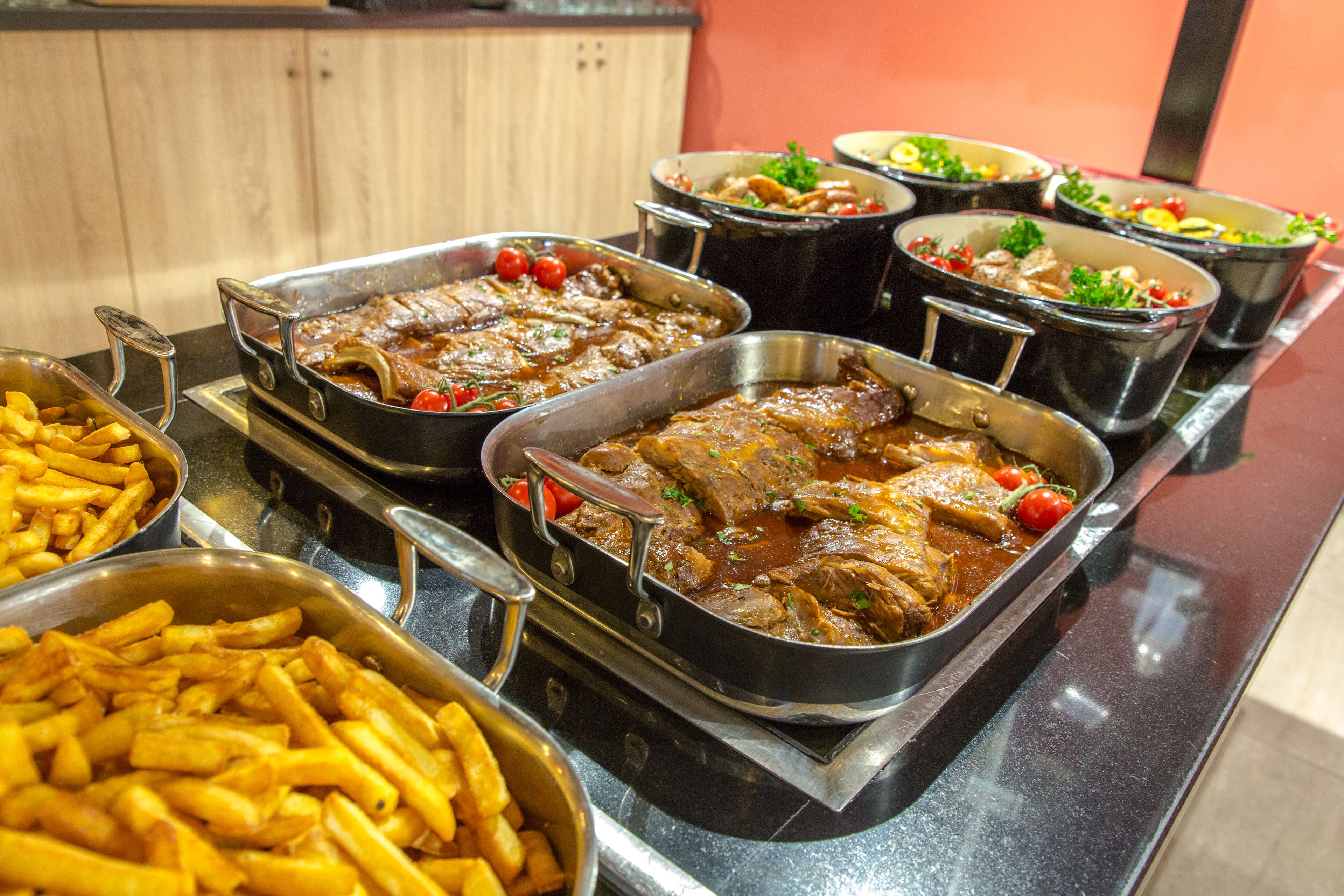 A buffet with various dishes including meat, vegetables, and fries.