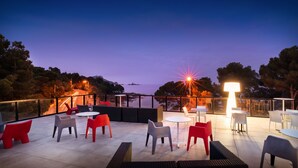 An outdoor terrace with seating and tables, overlooking a body of water and trees.