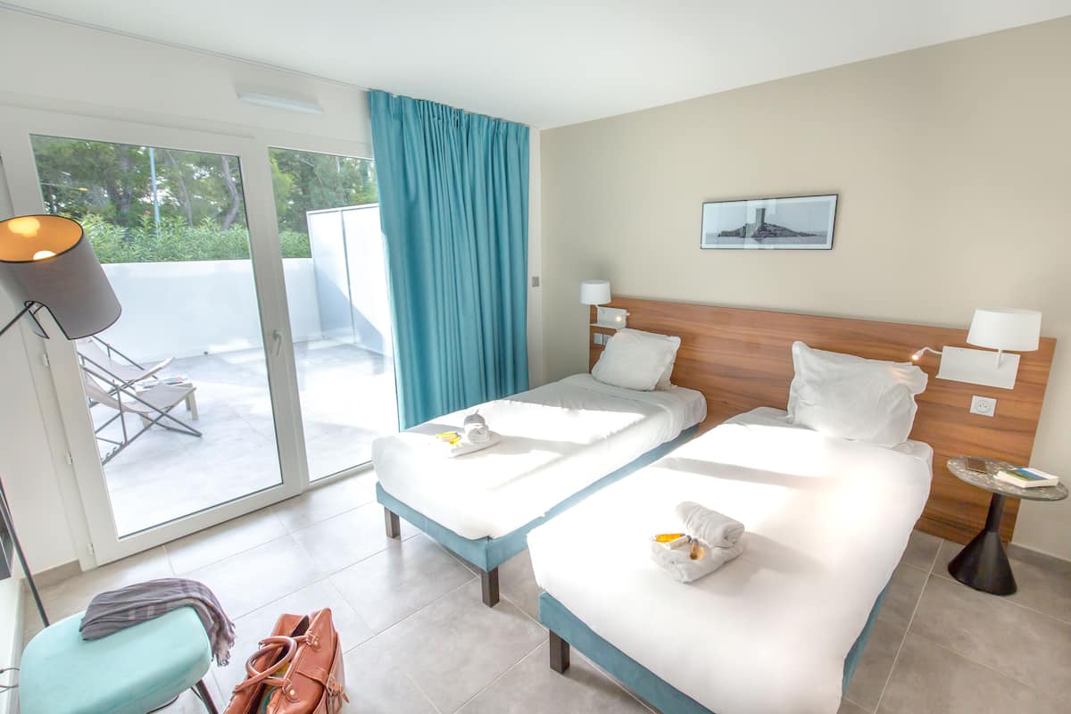 Habitación de hotel con dos camas, un balcón, una silla y una mesa.