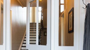 A hallway with a patterned floor, a white door, a staircase, and a plant in a basket. - Timoleague West Cork Priory House  (Cork)