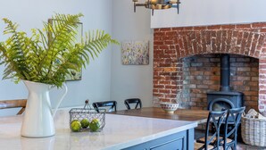 A kitchen with a brick fireplace, a hanging light fixture, and a white vase with green plants. - Timoleague West Cork Priory House  (Cork)