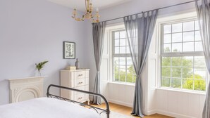 A bedroom with a bed, a dresser, a chandelier, and a window with curtains. - Timoleague West Cork Priory House  (Cork)