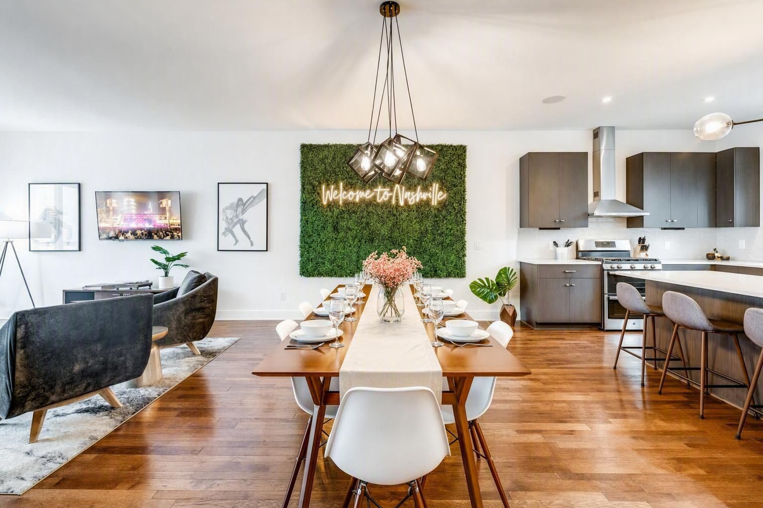 A modern kitchen with a dining area, wooden flooring, and a green wall with a neon sign.