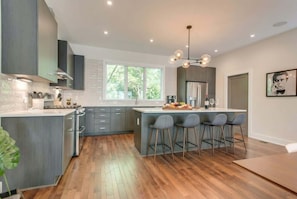 A modern kitchen with grey cabinets, a central island with bar stools, a large window, and a chandelier.