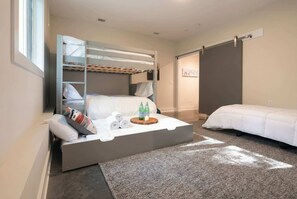 A modern hotel room with a bunk bed, a sofa bed, and a small table with bottles and towels.