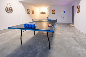 A ping pong table with blue accents, a 'Beer Cave' sign, and a 'BAR' sign in a room with a concrete floor.