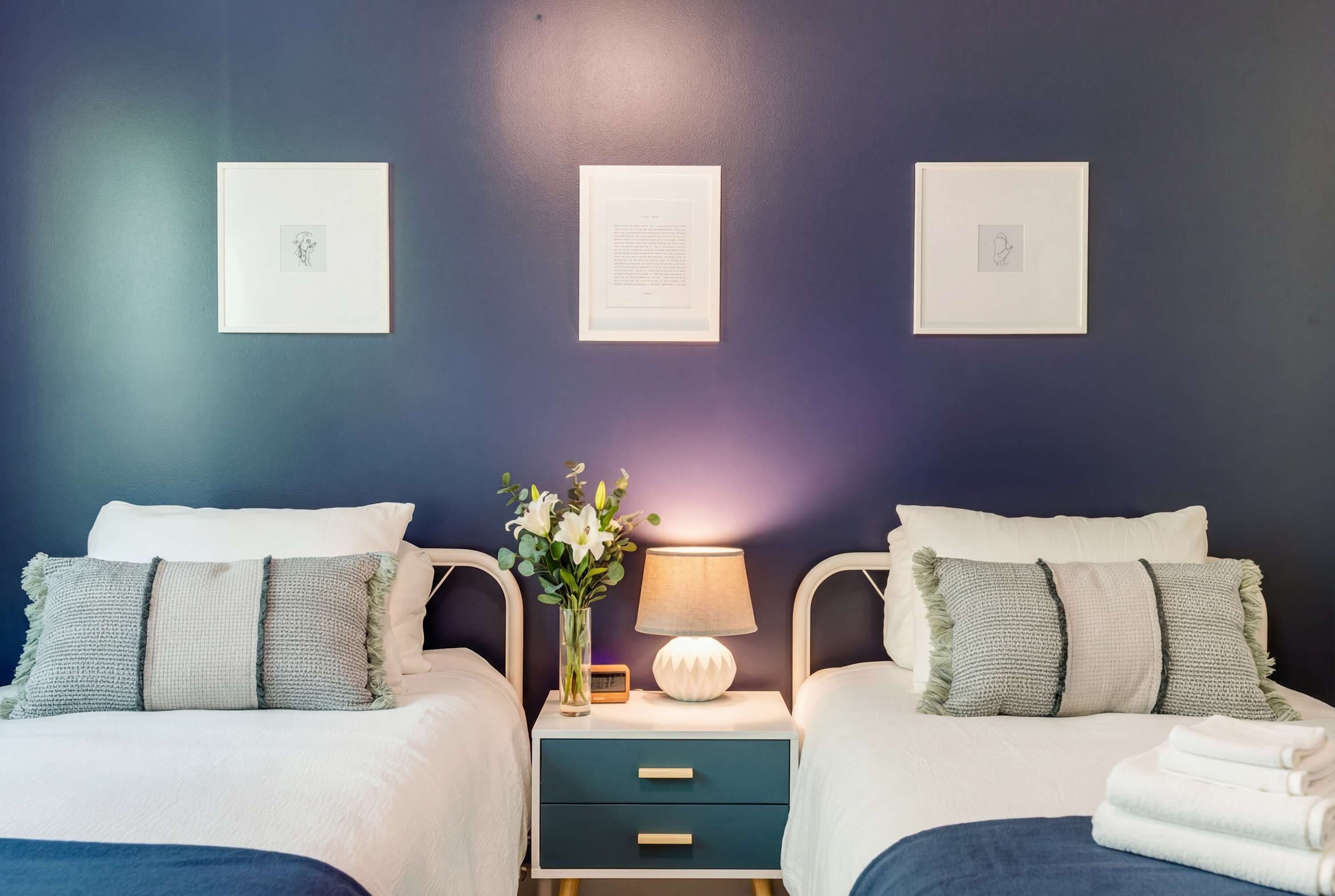 A bedroom with two beds, a nightstand with a lamp, and framed pictures on the wall.