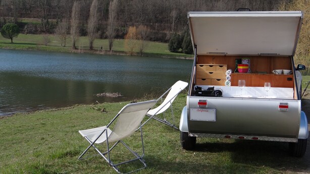 Een camper met open achterkant, waar een keukenruimte zichtbaar is met een spoelbak, kookplaat en opslagplanken.