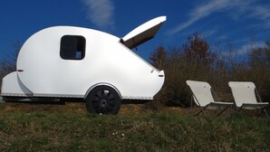Een witte recreatiewagen met open dak, geparkeerd op gras met twee opklapbare stoelen in de buurt.