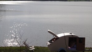 Een kleine, open trailer aan een meer, met daarin een persoon, een stoel en een tafel.