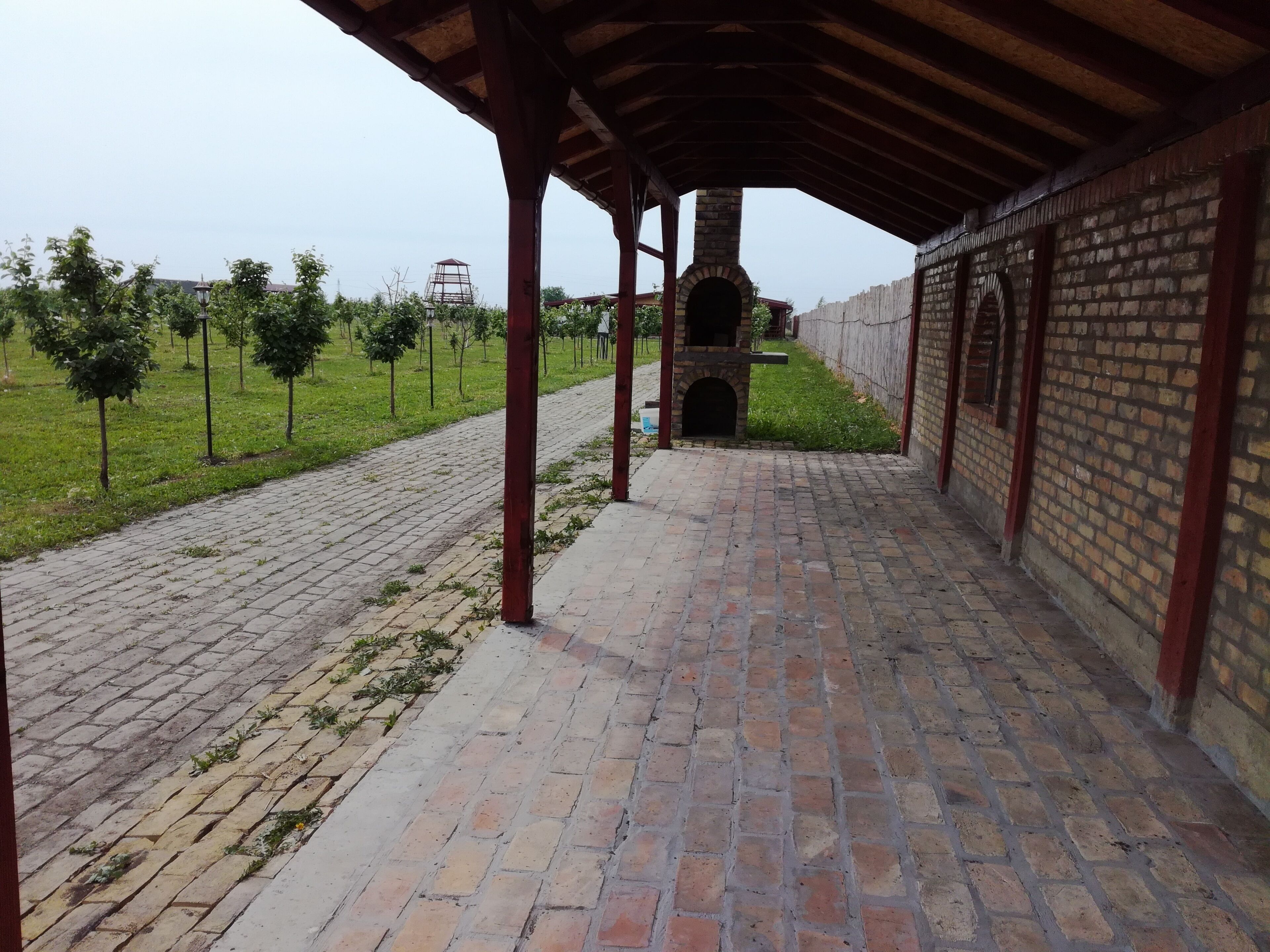 A covered brick patio with a brick oven, a wooden fence, and a grassy area with trees.