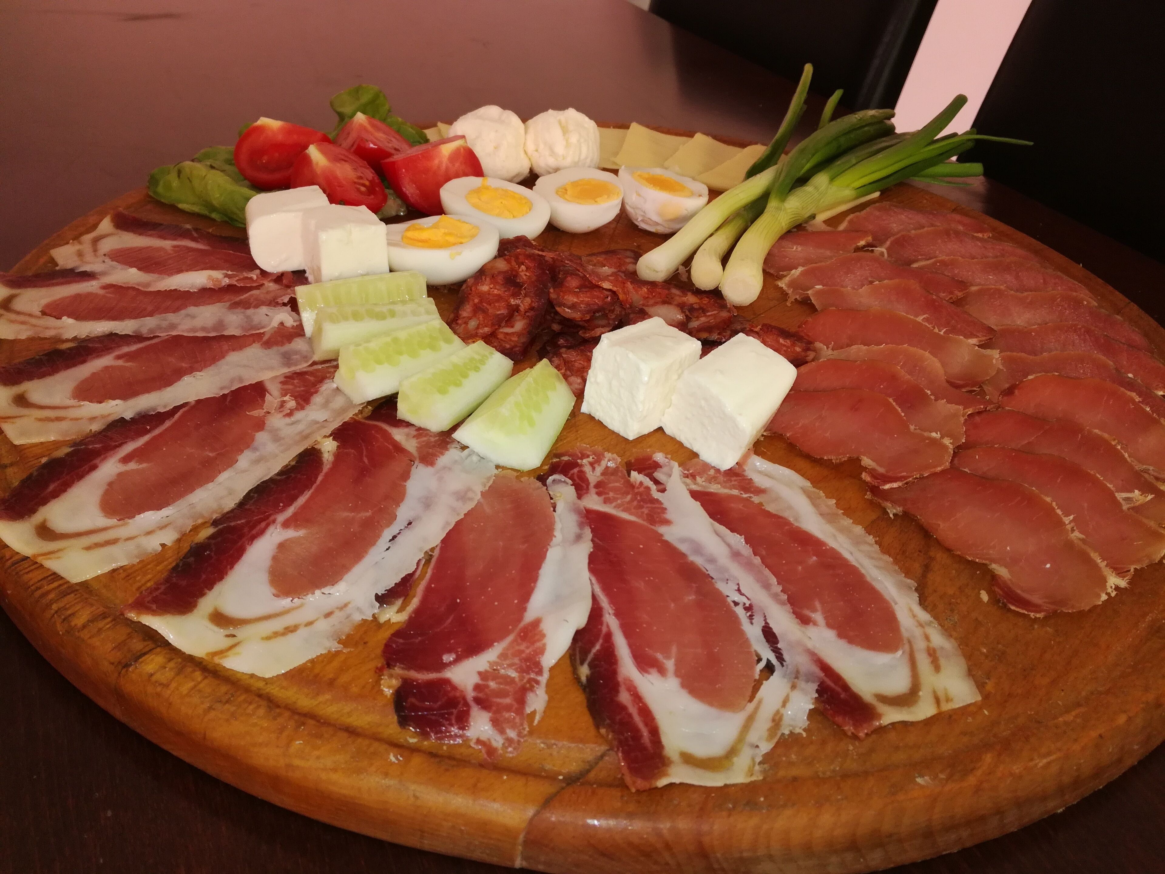 Ein Holzbrett mit verschiedenen Speisen, darunter Aufschnitt, Käse und Gemüse.