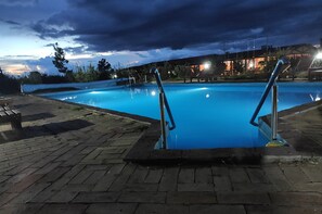 Piscina com grades de metal, rodeada por um pátio de tijolos.