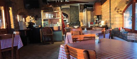 A cozy restaurant with checkered tablecloths, wooden chairs, and stone walls.