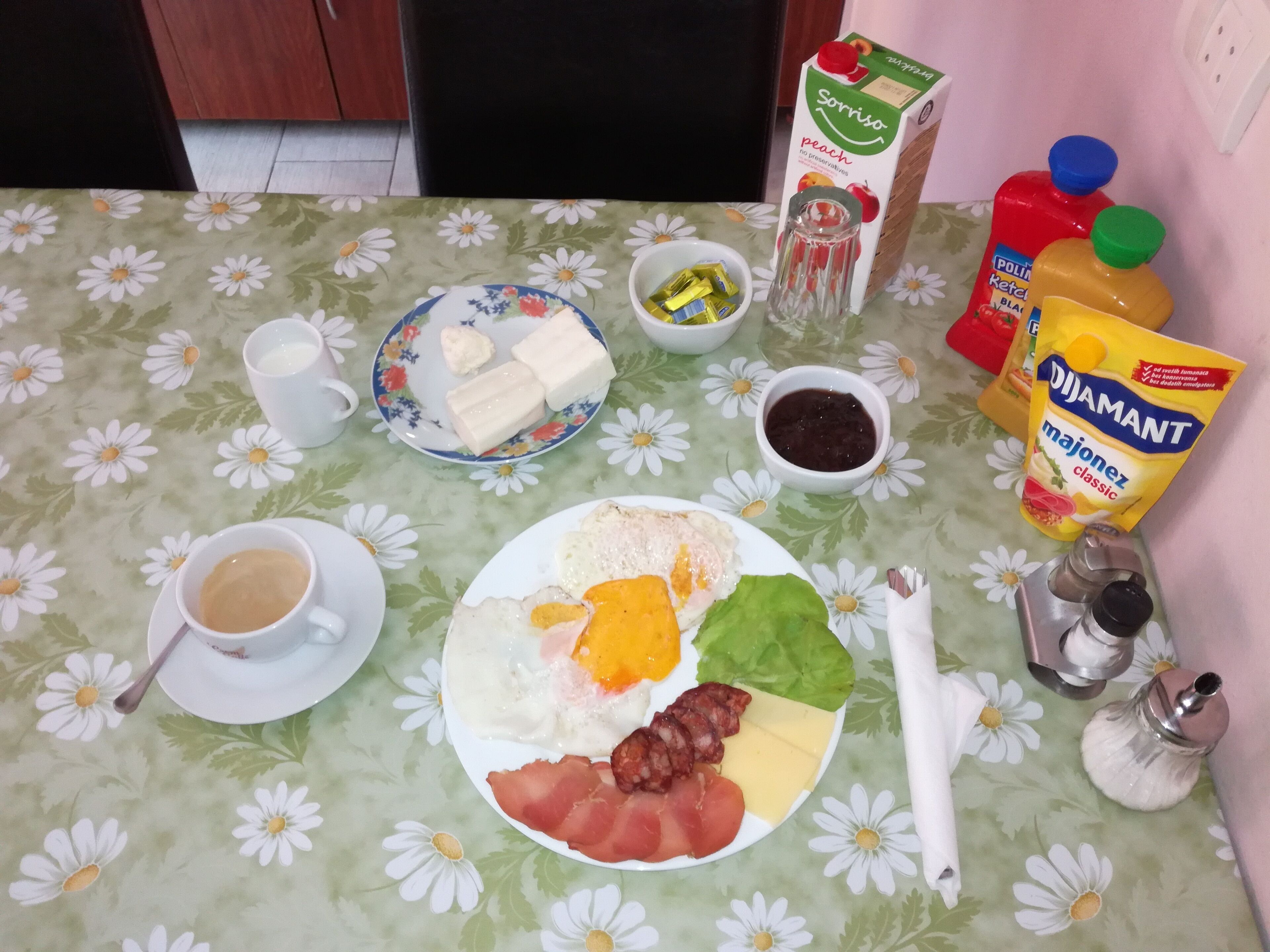 Ein Frühstückstisch mit Eiern, Speck, Käse, Gemüse, einer Kaffeetasse sowie verschiedenen Gewürzen und Aufstrichen.