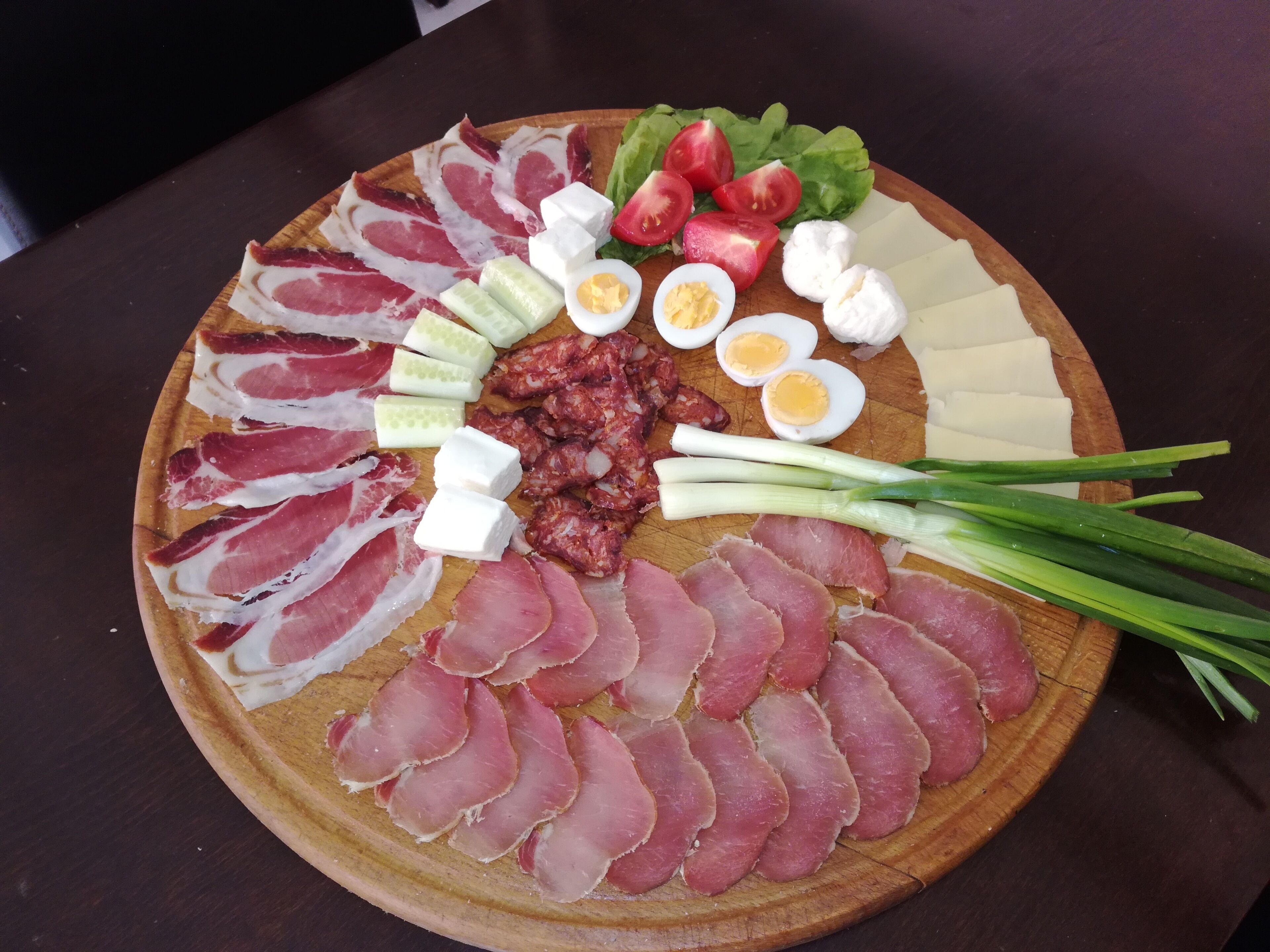 A wooden board with various food items including sliced meats, vegetables, and cheese.