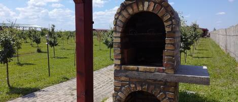 Un horno de ladrillo al aire libre con un estante de piedra, rodeado de césped y un sendero pavimentado.