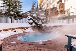 Ein Whirlpool, umgeben von Schnee, mit einer Steinmauer und einem Holzzaun.