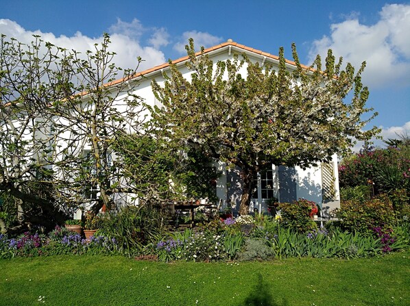 A white building with a tiled roof, surrounded by a well-maintained garden with various plants and flowers.