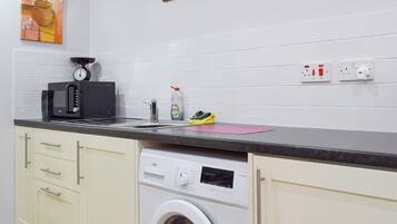 Uma cozinha compacta com máquina de lavar, micro-ondas e pia.