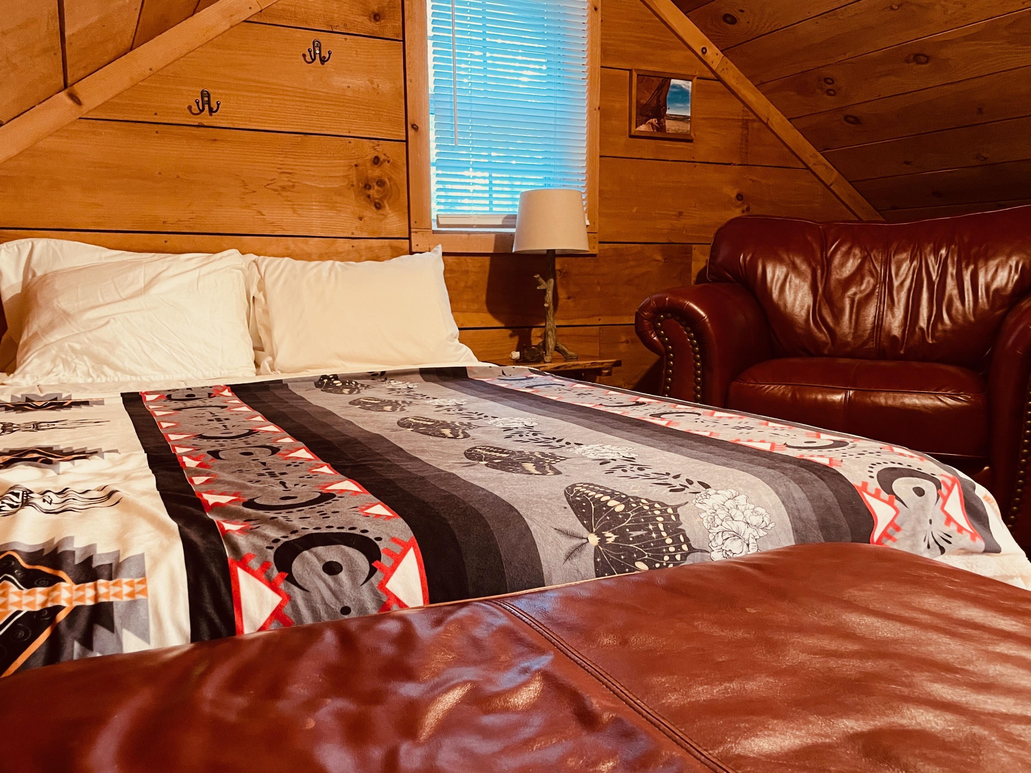 Een gezellige kamer met een bed, een leren fauteuil en een raam met zonwering.