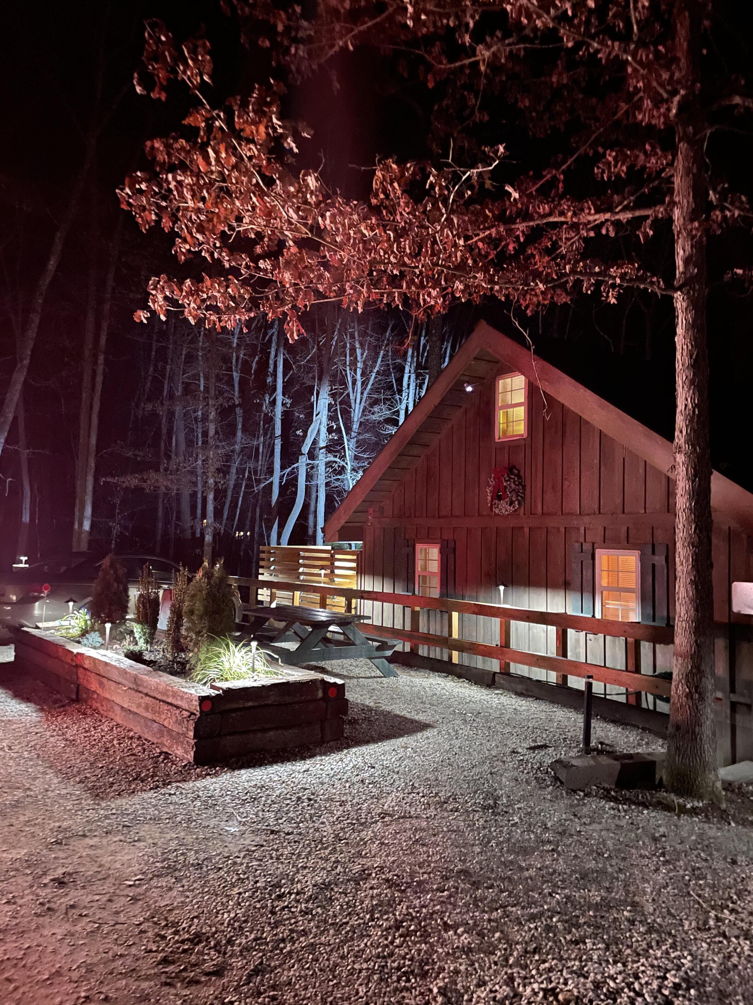 Un chalet rustique avec une façade en bois, une allée en gravier et un banc placé sous un arbre.